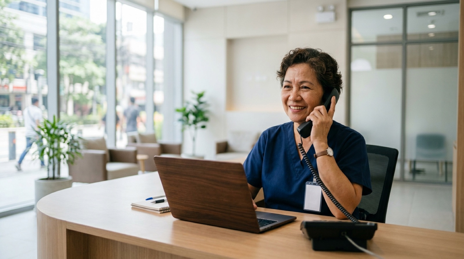 Clinic receptionist smiling while taking a phone call at the front desk